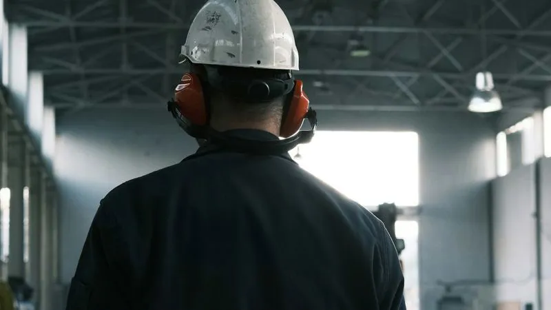 Addetto con casco e abbigliamento da lavoro all'interno di uno stabilimento produttivo